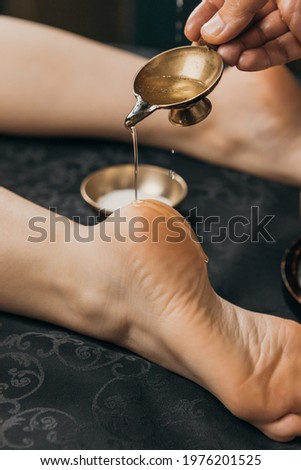 Close-up of hand pouring oil on foot. Oil applicator for relaxing massage. Gold body treatment and diamond powder exfoliating scrub.