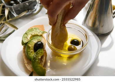 Close-up of hand preparing avocado toast with olive oil and black olives. A delicious and fresh snack on a white plate. - Powered by Shutterstock