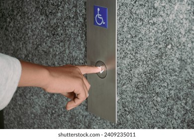 Close-up hand pressing the button for the disabled elevator to go down the building.