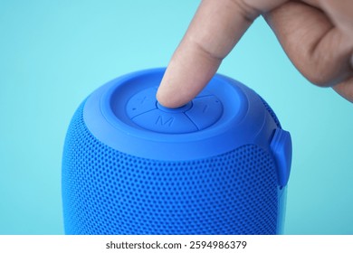 Close-up of a hand pressing a button on a portable blue speaker