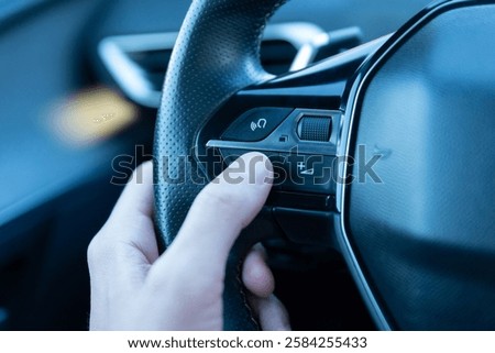 Close-up of a hand pressing the voice command button on a steering wheel, showcasing smart car technology, AI-driven assistance, and hands-free driving innovation