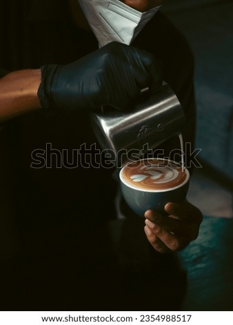 Close-up of the hand of a professional barista in a coffee shop making latte art on a cup of cappucino with green cup 