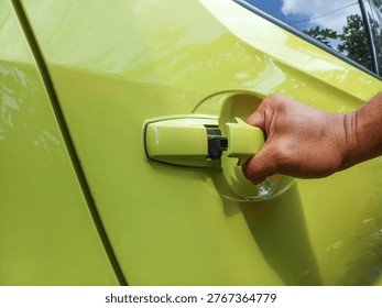 Close-up of a hand pulling a lime green car door handle. Opening vehicle door concept for automotive, transportation, safety, and security stock photography.