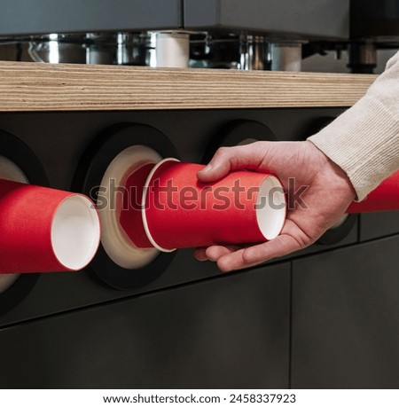 Close-up of a hand pulling a red paper cup from a modern cup dispenser in a cafeteria setting