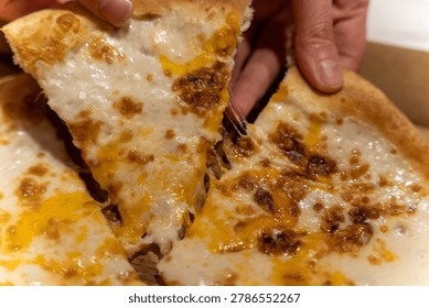 Close-up of a hand pulling a slice of cheesy pizza with melted cheese and toppings, showcasing a delicious, appetizing view of the pizza in a cardboard box