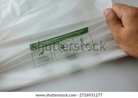 Close-up of a hand pulling a white plastic bag with a green eco label on a light background.