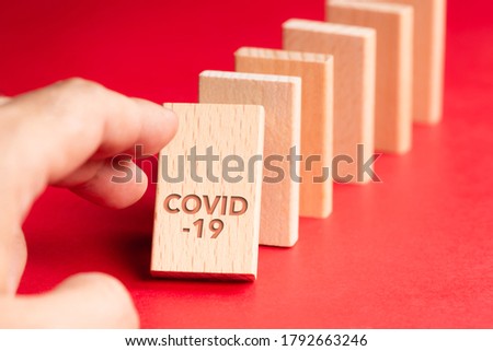 Closeup hand push the first domino of Covid-19 and going to fall down to the others, consequences of Covid-19 pandemic