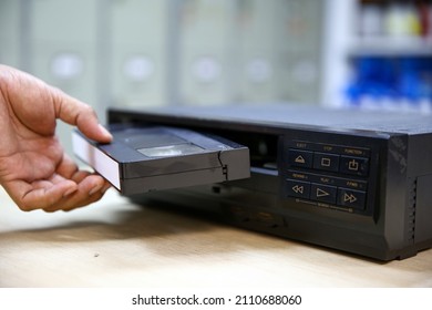Close-up hand put or insert video cassette tape VHS old retro style stack on video record player concept of vintage electric and electronic appliances multimedia player device old fashioned.