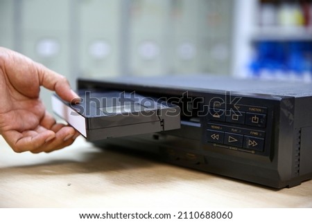 Close-up hand put or insert video cassette tape VHS old retro style stack on video record player concept of vintage electric and electronic appliances multimedia player device old fashioned.