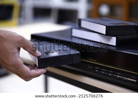 Close-up hand put or insert video cassette tape VHS old retro style on video record playback concept of vintage electric and electronic appliances multimedia player device old fashioned.