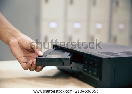 Close-up hand put or insert video cassette tape VHS old retro style on video record playback concept of vintage electric and electronic appliances multimedia player device old fashioned.