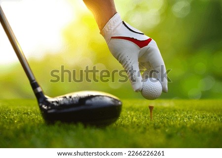 Close-up hand putting golf ball on tee with drivers.