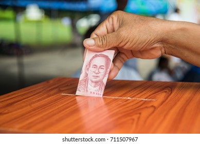 Closeup hand putting Thai money into a wooden  donation box in Temple.