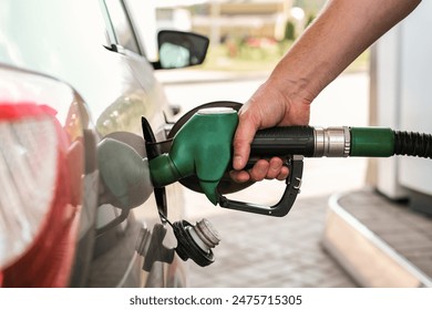 Close-up of a hand refueling a car with a green nozzle at a gas station - Powered by Shutterstock