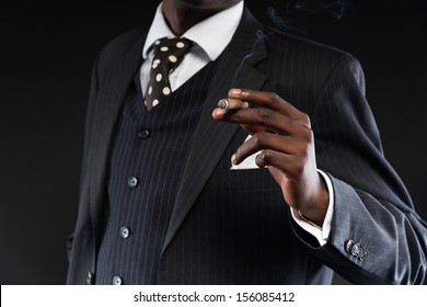 Close-up of hand of retro african american mafia man wearing striped suit and tie. Smoking cigar. Studio shot. - Powered by Shutterstock