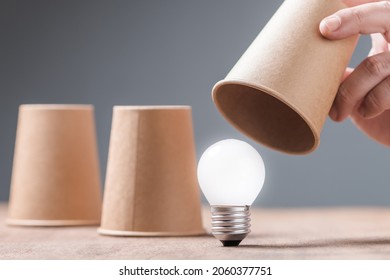 Closeup hand reveal where the light bulb is in three cups shell game, helpful tips, reveal the success idea concept, or FAQs - Shutterstock ID 2060377751