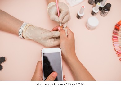 Close-up Of A Hand. In The Salon Of Gel Manicure, The Process Of Drying Gel On Nails, Beauty And Personal Care, Modern Technologies. Work With Gloves. Set Of Nails, Hold The Phone