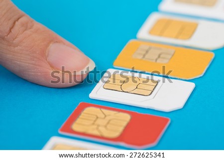 Close-up Of Hand Selecting Sim Card Over Blue Background