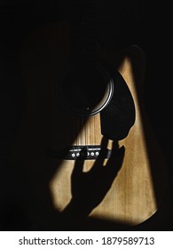 A closeup of a hand shadow strumming on guitar strings