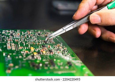 Close-up of hand with silver tweezers replacing electrical components on complex surface of circuit board. Modern technology. Repairing by hand. Horizontal shot. High quality photo
