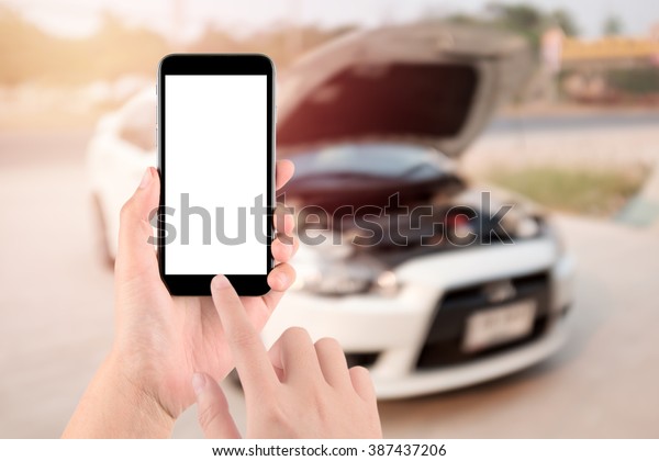closeup of\
hand with smartphone a white screen on broken car\
background.transportation,  vehicle concept \
