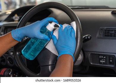 Closeup Of Hand Spraying A Blue Sanitizer From A Bottle For Disinfecting Steering Wheel In A Car.Antiseptic,disinfection ,cleanliness And Healthcare,Anti Bacterial And Corona Virus (COVID-19)