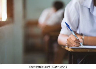 Closeup To Hand Of Student  Holding Pen And Taking Exam In Classroom With Stress For Education Test.