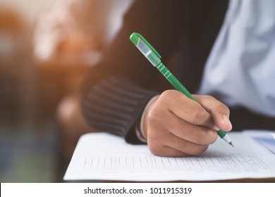 Closeup To Hand Of Student  Holding Pen And Taking Exam In Classroom With Stress For Education Test.