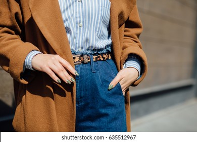 Closeup of hand of stylish woman in brown coat blue striped shirt, blue jeans with tiger pattern belt. Fashionable girl on the street. Female fashion