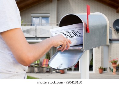 Close-up Of Hand Taking Newspaper From Mailbox In Front Of Their House