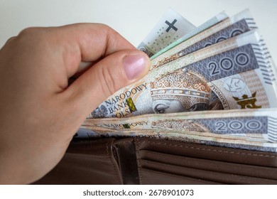 Close-up of a hand taking out multiple 200 złoty banknotes from a brown leather wallet