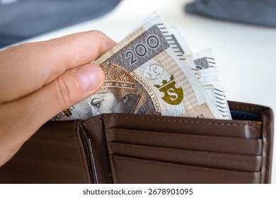 Close-up of a hand taking out multiple 200 złoty banknotes from a brown leather wallet