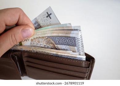 Close-up of a hand taking out multiple 200 złoty banknotes from a brown leather wallet