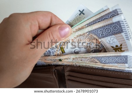 Close-up of a hand taking out multiple 200 złoty banknotes from a brown leather wallet