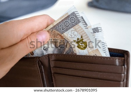 Close-up of a hand taking out multiple 200 złoty banknotes from a brown leather wallet