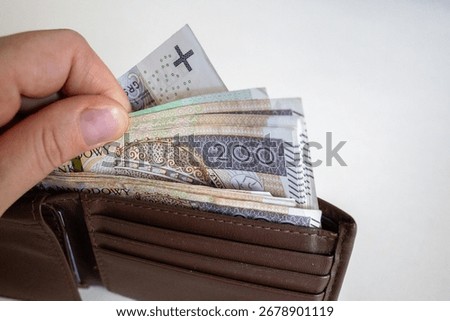 Close-up of a hand taking out multiple 200 złoty banknotes from a brown leather wallet