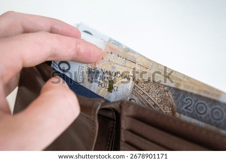 Close-up of a hand taking out multiple 200 złoty banknotes from a brown leather wallet