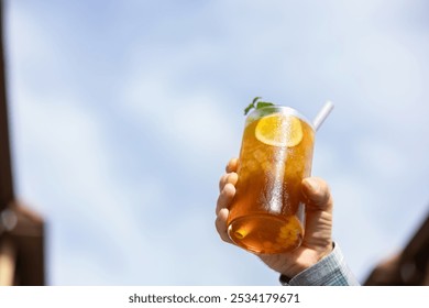 Close-up hand taking a pina colada tea cocktail with peach balls, orange or lemon slice and mint, mocktail, refreshing and healthy drink, blue sky background free to write, copy space - Powered by Shutterstock