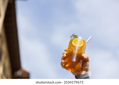 Close-up hand taking a pina colada tea cocktail with peach balls, orange or lemon slice and mint, mocktail, refreshing and healthy drink, blue sky background free to write, copy space - Powered by Shutterstock