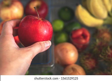 Close-up Hand Taking Red Apple From Fridge With Assorted Of Vegetables And Fruits As A Background.