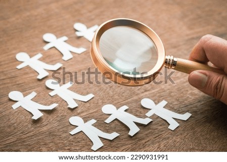 Closeup hand that hold the magnifying glass over the paper human dolls, find a right person, leadership, talent people, and recruitment, HR concept