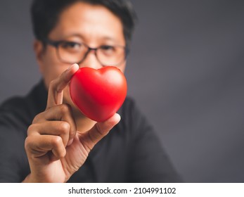 Close-up Of Hand Tomboy Holding A Red Heart While Sitting Against A Gray Background. Tomboy, A Girl Who Loves To Be A Man. LGBT, Gender Equality Act, Love, Valentine's Day Concept