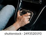 Close-up hand of unrecognizable driver male moving lever arm on gearbox to add speed. Closeup top view of man sitting on driver seat shifting automatic transmission in car