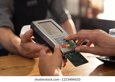 Closeup Of Hand Using Credit Card Swiping Machine To Pay. Female Hand With Credit Card Paying Through Terminal For Payment In Coffee Shop. Woman Entering Debit Card Code In Swipe Machine.