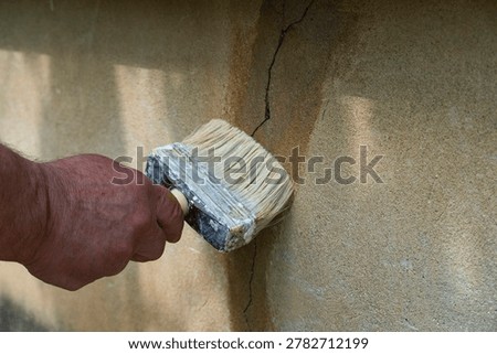 Close-up of a hand using a large paintbrush to seal and repair a cracked plaster wall, symbolizing home maintenance, construction work and DIY improvement