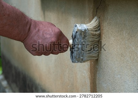 Close-up of a hand using a large paintbrush to seal and repair a cracked plaster wall, symbolizing home maintenance, construction work and DIY improvement