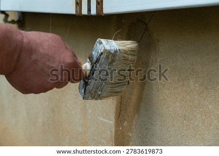Close-up of a hand using a large paintbrush to seal and repair a cracked plaster wall, symbolizing home maintenance, construction work and DIY improvement