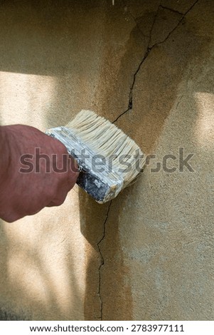 Close-up of a hand using a large paintbrush to seal and repair a cracked plaster wall, symbolizing home maintenance, construction work and DIY improvement