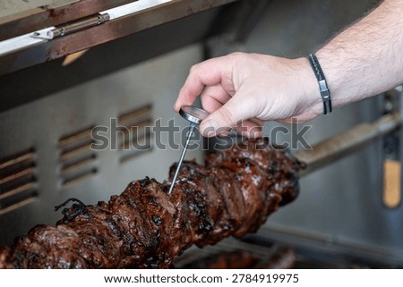 Close-up of a hand using a meat thermometer to check the temperature of grilled meat on a rotisserie for perfect cooking.