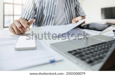 Close-up of hand using mobile phone with documents and working on laptop to searching for information to start own business, concept for working at home, start new business